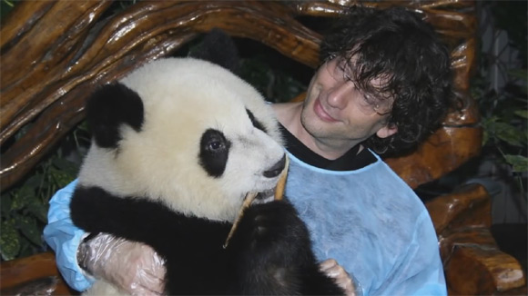 Neil Gaiman trzyma na kolanach małą pandę podczas wizyty w Pekinie w 2009 roku.